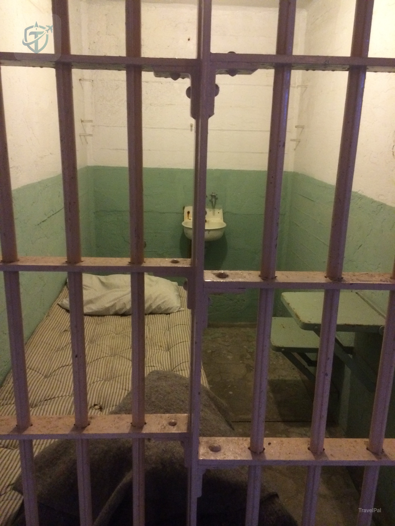 Small Alcatraz prison cell with a bed, sink, and toilet behind metal bars