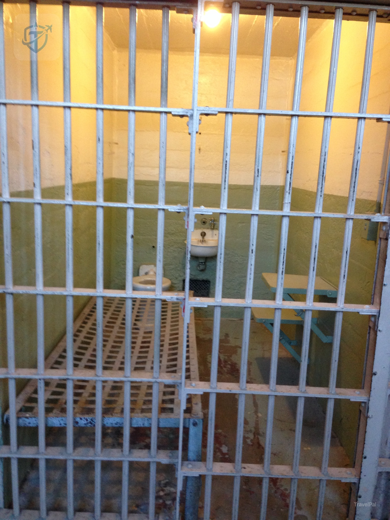 Alcatraz cell with a narrow bed and sink seen through a metal door