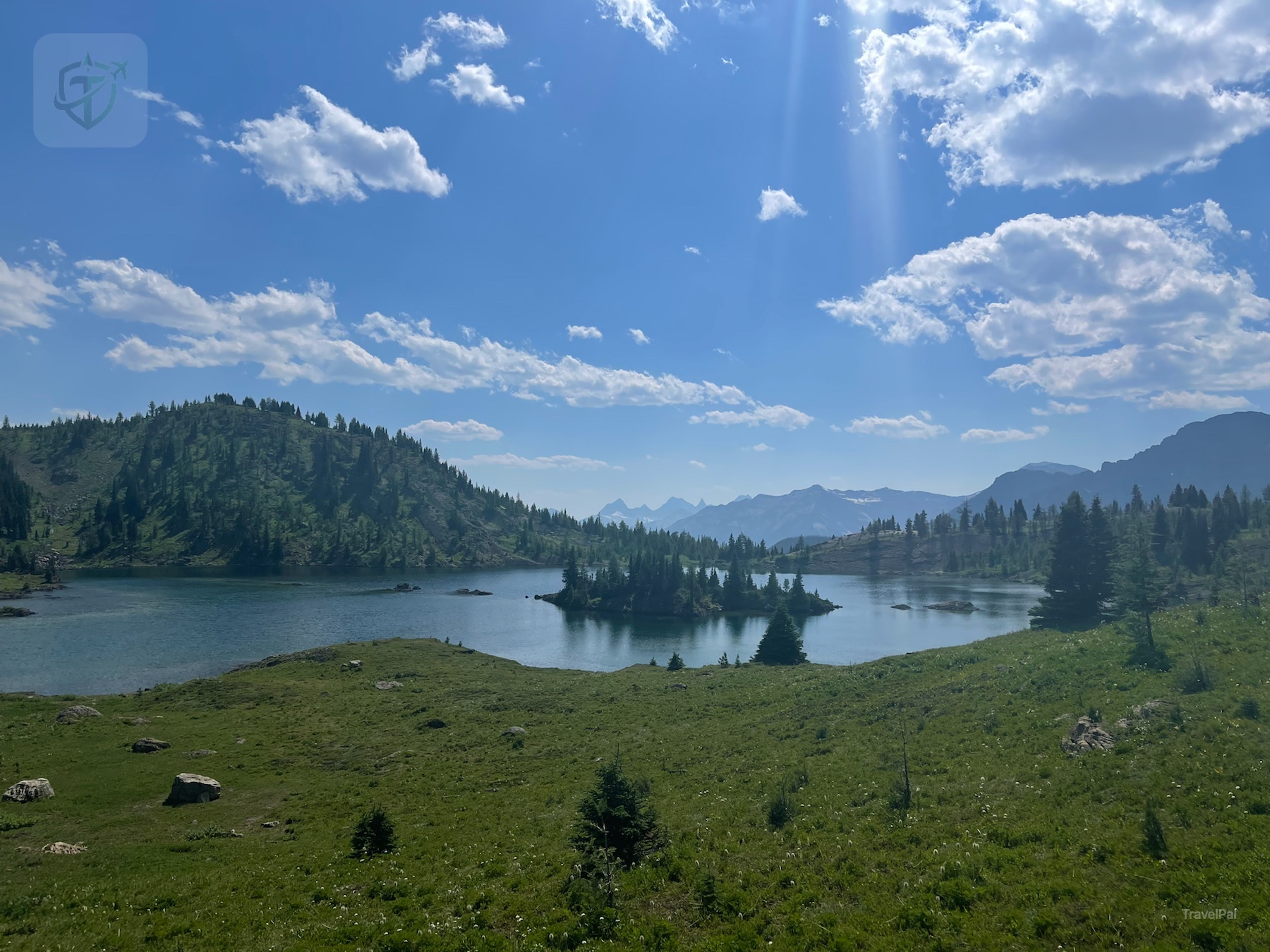Blue alpine lake with a small tree-covered island and mountains at Sunshine Meadows