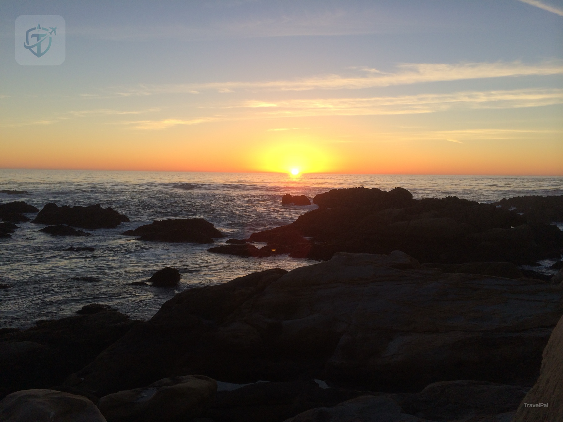 Sunset over the Pacific Ocean behind dark coastal rocks