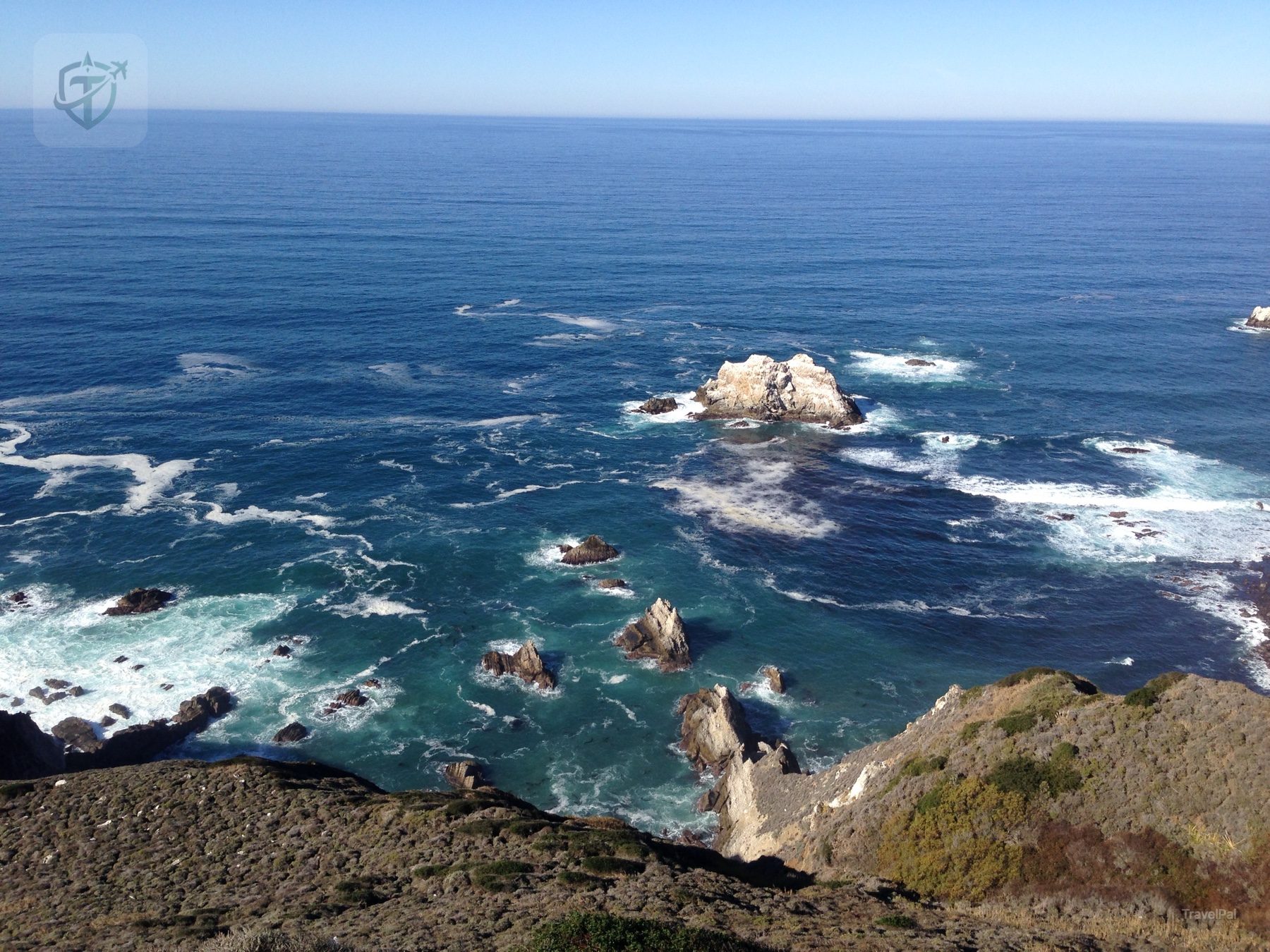 White surf curling around isolated rocks below a high California coastal overlook