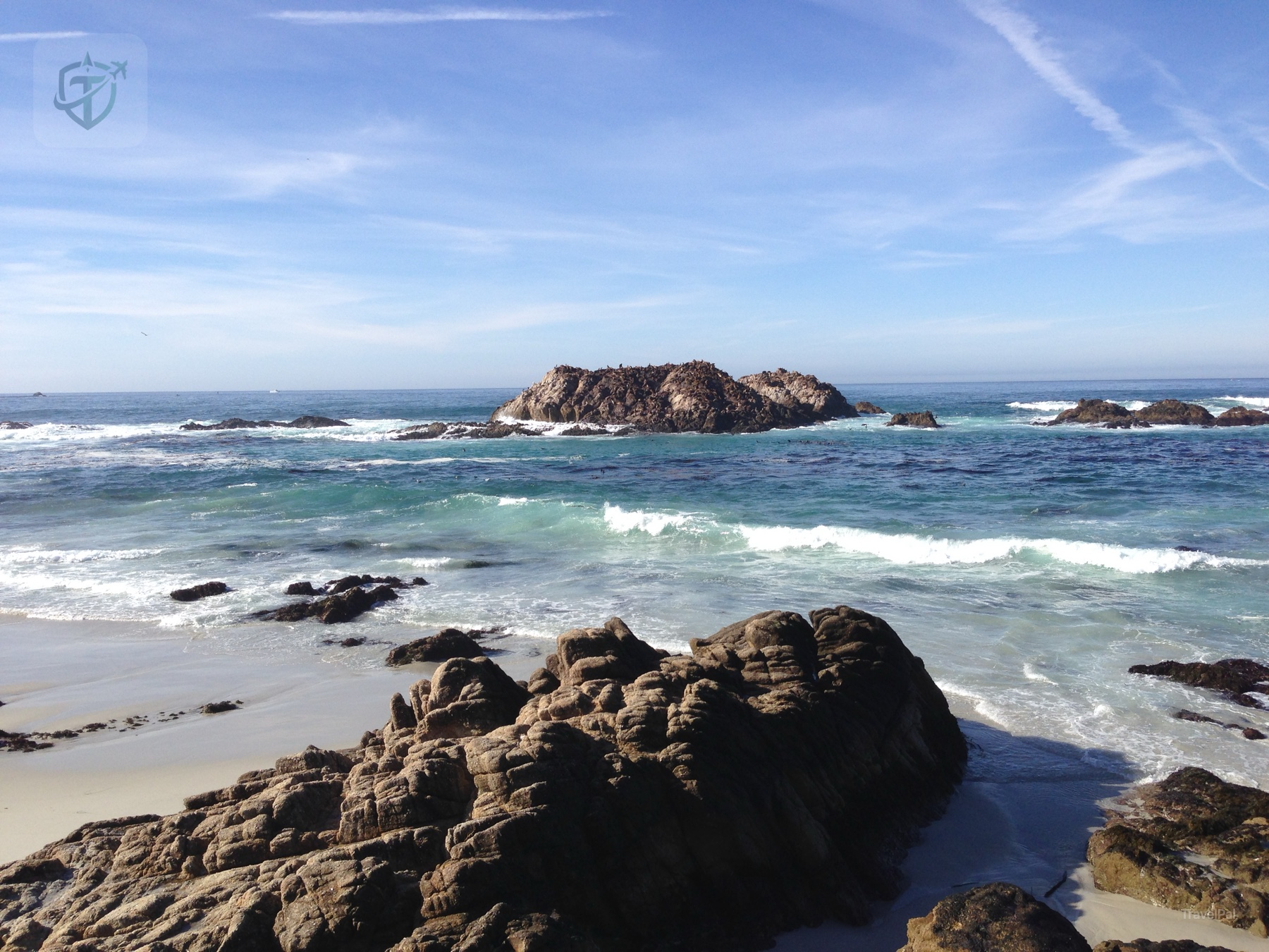 Low sea rocks surrounded by white surf and a clear Pacific horizon