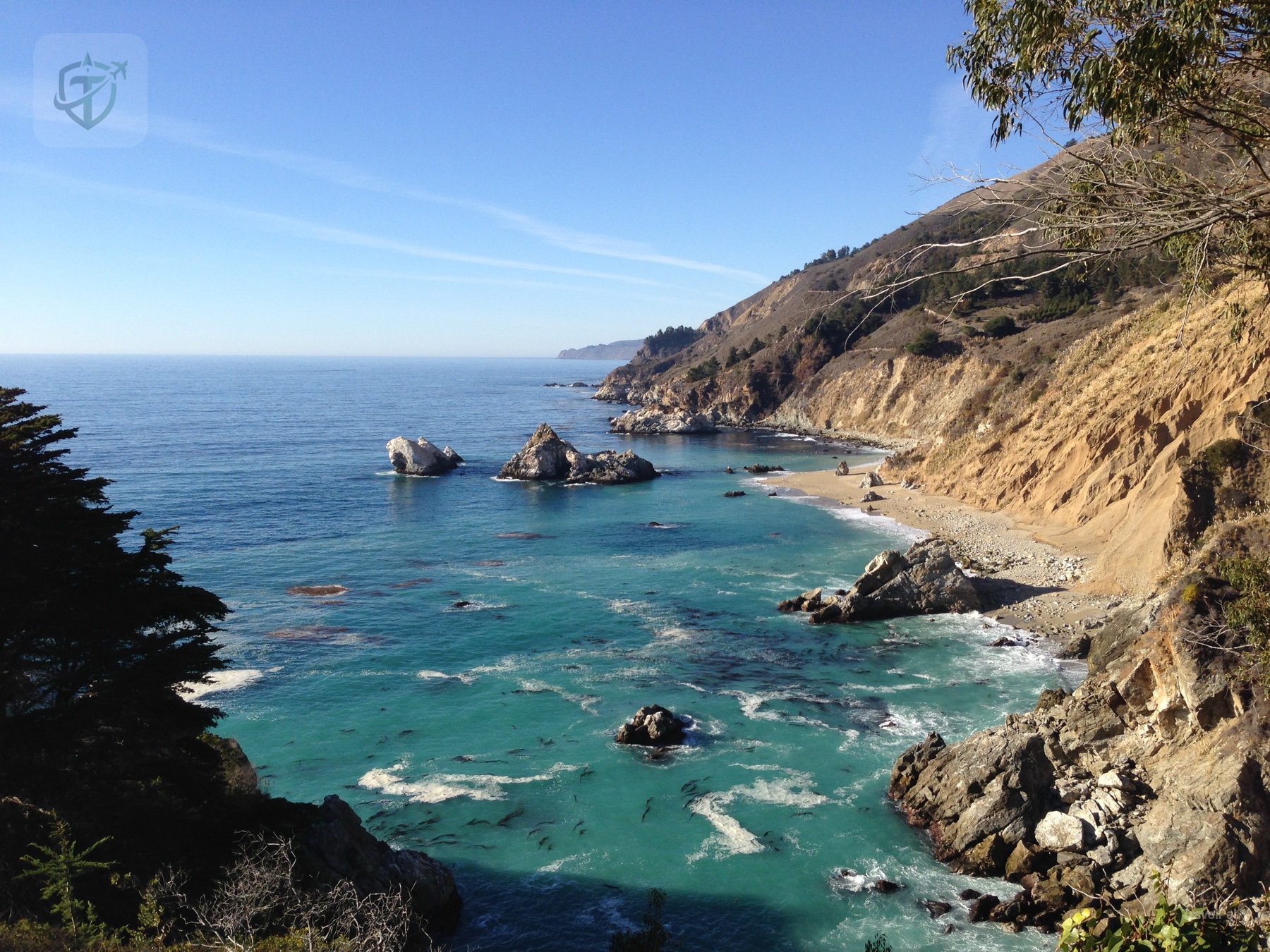 Turquoise cove and rounded sea rocks beneath a California coastal hillside