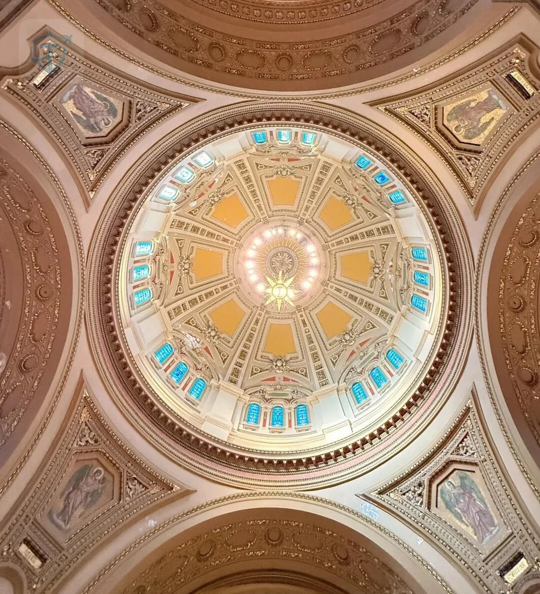 Warm cream and gold interior dome with stained glass and an eight-pointed chandelier