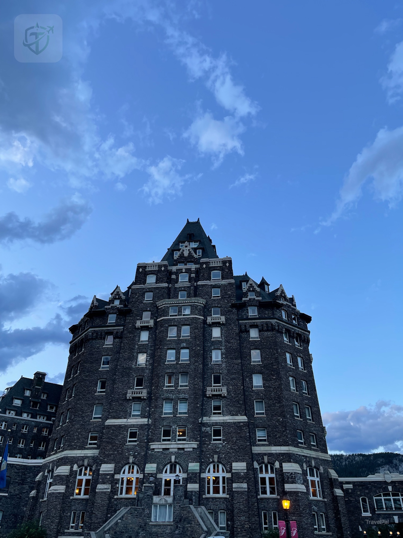 Tall central tower of Fairmont Banff Springs framed by blue evening sky and mountain foothills