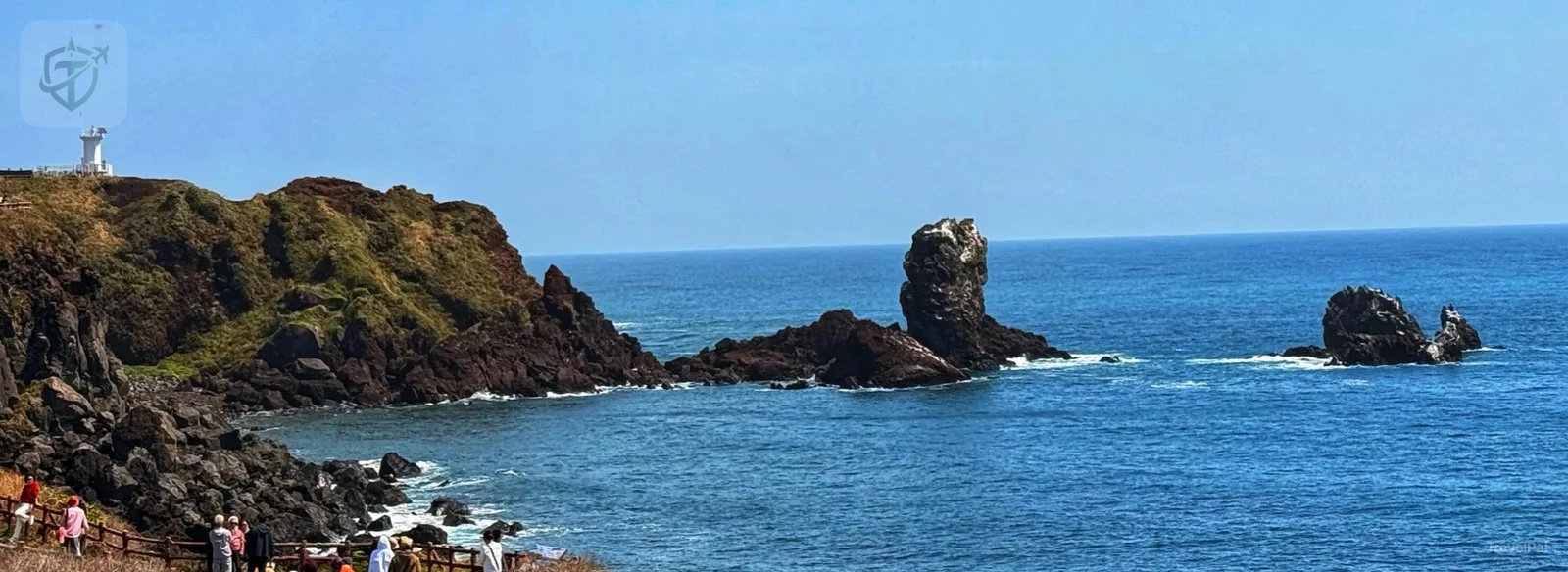 Dark volcanic rocks, blue sea, and a white lighthouse on Jeju's east coast