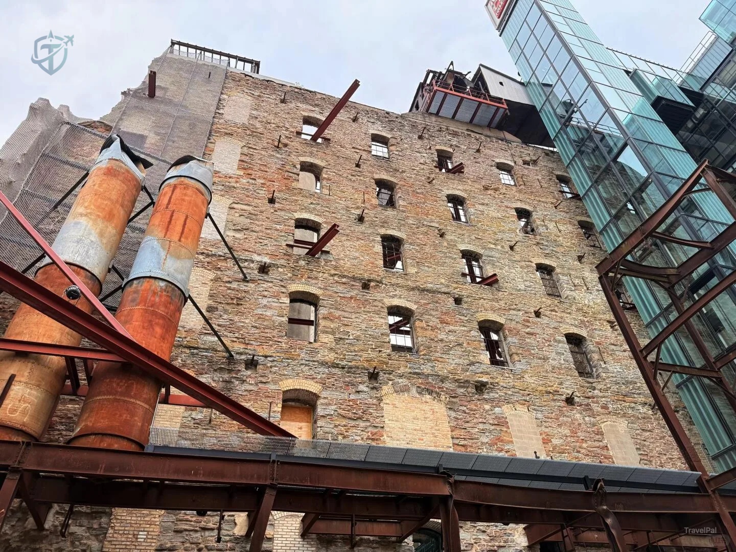 Stone wall, rusted pipes, and modern glass structures at the Mill City ruins