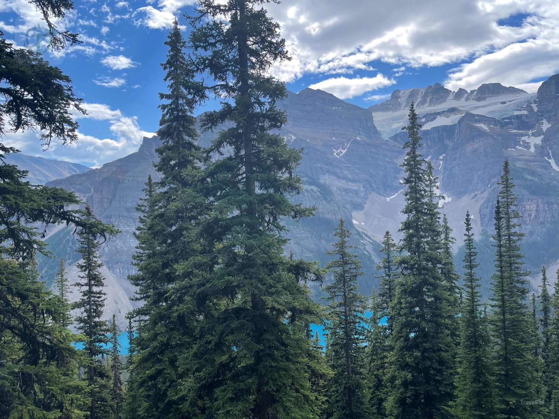 Evergreen forest framing a turquoise lake and mountain wall on the Sentinel Pass approach