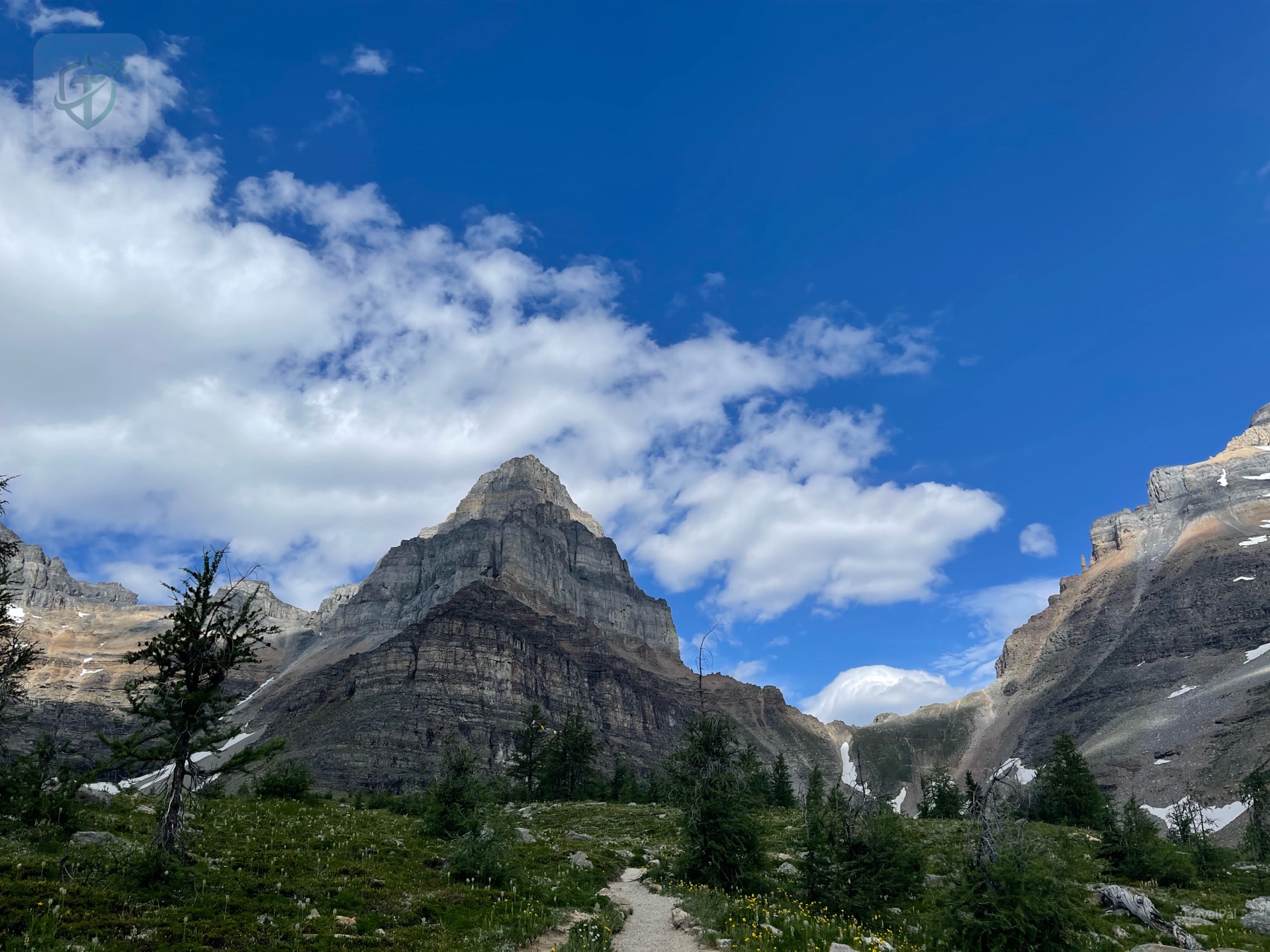 A narrow trail crossing an open alpine meadow beneath jagged peaks