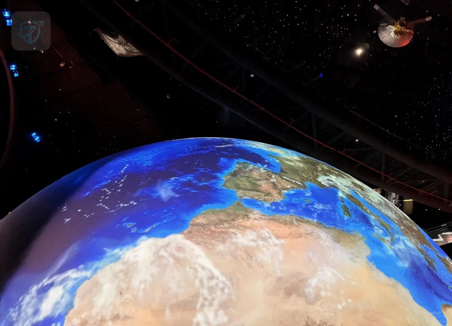 Large illuminated Earth visualization beneath hanging spacecraft